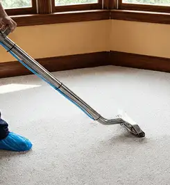 Steam carpet cleaning technician using a hot-water extraction wand on a residential carpet, wearing blue protective shoe covers Richmond, VA.