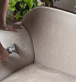 Professional upholstery cleaner deep-cleaning a fabric sofa with a handheld extraction tool and hose Richmond, VA.