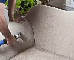Professional upholstery cleaner deep-cleaning a fabric sofa with a handheld extraction tool and hose in Richmond, VA.